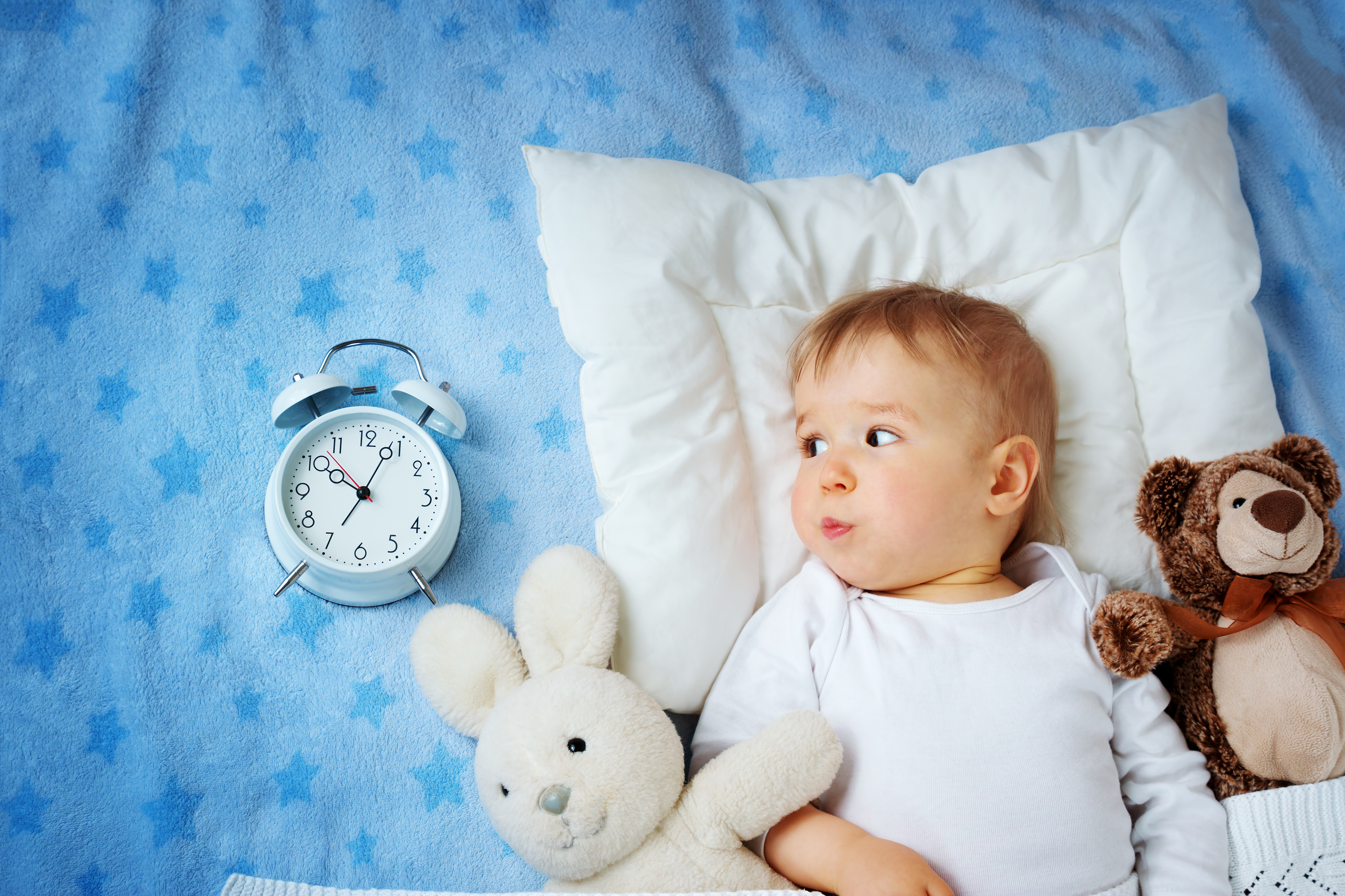 One year old baby lying in bed with alarm clock