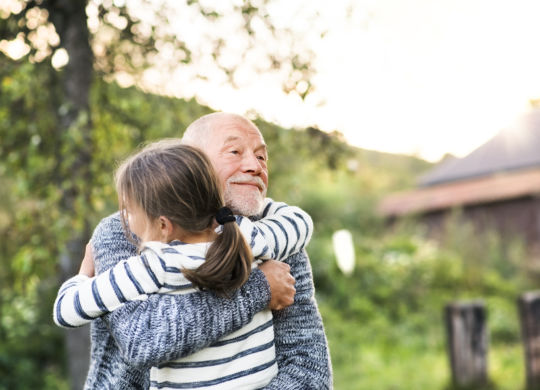 Grandfather giving his grandaughter a hug. Senior man and a small girl enjoying time in nature.