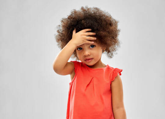 childhood and people concept - sad little african american girl touching her forehead over grey background