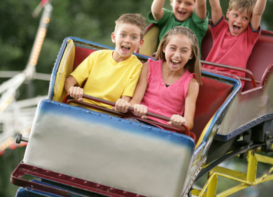 Young kids riding an amusment park roller coaster at the county fair.