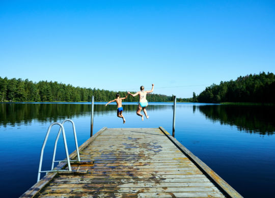 Frau und Kind springen in Bade See vom Steg aus im Familienurlau