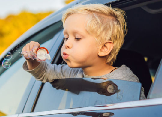 Boy blowing bubbles in the car window. Traveling by car with children.