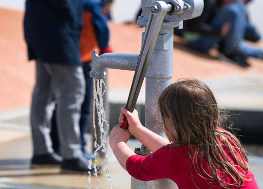 Kind liebt Wasser und spielt am Wasserspielplatz mit der Familie