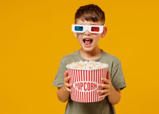 Littl surprised boy 6-7 years old in 3d glasses green t-shirt watch movie film hold takeaway popcorn bucket look camera isolated on yellow background studio portrait People emotions in cinema concept.