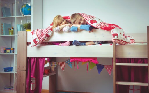 Two happy sibling children having fun in bunk bed under blanket