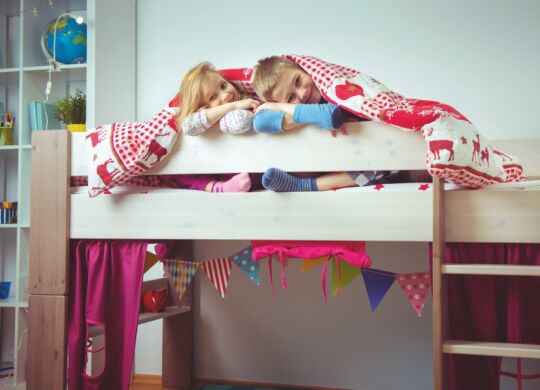 Two happy sibling children having fun in bunk bed under blanket